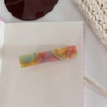 Macro shot of colorful acetate hair claw with iridescent marble texture on cream notebook - Orange Duckbill Clip