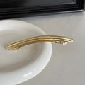 Nahaufnahme einer minimalistischen goldenen Haarspange auf einem weißen Keramikteller - Gold