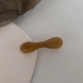 Detailed view of an amber bow-shaped acetate hair clip on a minimalist textured background - Gradient Coffee
