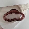 Vue détaillée de la pince à cheveux en résine ambrée aux lignes fluides ondulées - Marron