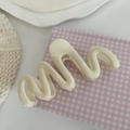 Dettaglio della pinza per capelli color crema a onde su sfondo estetico curato - Bianco Crema