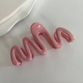 Dettaglio molletta per capelli rosa ondulata con finitura lucida su sfondo minimalista - Rosa crema