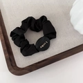 Detail of black satin hair scrunchie with Lucky golden oval buckle on linen tray - Black - Round