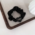 Detail of black satin scrunchie featuring a matte heart charm with golden Lucky text - Black-Heart