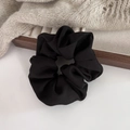 Detail of high-elasticity black satin scrunchie displayed on a warm wooden stand - Black