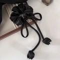 Detail view of a black satin hair scrunchie with elegant tulip ribbon on a wooden box - Black