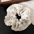 Gros plan sur un chouchou floral beige avec dentelle délicate et petit détail d'étiquette M - Floral Café