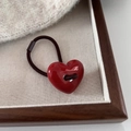 Primer plano de un colgante de corazón rojo brillante en un coletero marrón grueso - Corazón