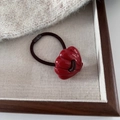 Close-up of a red shell-shaped resin charm on an elastic hair tie in a wooden tray - Shell