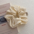 Close-up of cream textured scrunchie with a fabric label on a minimalist background - Beige