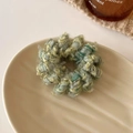 Primer plano de un coletero de tweed tejido en verde y amarillo sobre un plato de cerámica - Verde