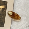 Close-up of amber tortoiseshell acetate oval hair clip with gold metal accent on white paper - Brown