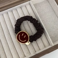 Détail d'un chouchou en velours marron avec un pendentif smiley en métal bordeaux - Style Pendentif Smiley / Bordeaux