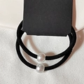 Dettaglio di due elastici per capelli neri con perle su sfondo in tessuto bianco testurizzato - Motivo Diagonale / Nero