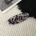 Detail shot of a large oval acetate hair clip with abstract gold foil textures on soft rug - Coconut Strip Pattern