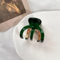 Detail of emerald green acetate hair claw clip with golden metal teeth on ceramic tray - Green