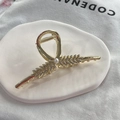 Detalle de la pinza para el cabello de espiga dorada con pedrería y perla central - Dorado