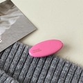 Rosa ovaler Haarclip mit Goldlogo auf grauem Strickstoff minimalistischer Entenschnabel - Rosenrot