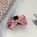 Detalle de pinza para pelo con lazo rosa y placa dorada sobre mesa color crema - Rosa