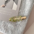 Close-up of green marble acetate hair clip with golden metal crocodile grip on grey fabric - Green