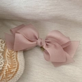 Detail von rosa geschichteter Netz-Haarspange mit Goldanhänger auf weißem Stoff - Rosa