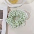 Detailopname van lichtgroene geruite scrunchie met witte kant op een dienblad - Groen