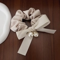 Dettaglio di uno scrunchie in raso crema con fiocco e ciondoli con perle dorate - Beige
