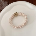 Close-up van beige geplooide scrunchie met hartvormige harskraal op keramiek dienblad - Beige