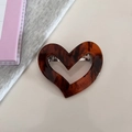 Detail of tortoise shell heart hair clip with silver spring mechanism on a table - Brown