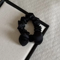 Detail of a black satin scrunchie with a ribbon bow on a white textured board - Black
