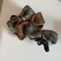 Detail showing tweed and plush bow texture on a dark green and brown banana hair clip - Green
