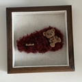Detalle de una pinza de pelo de peluche granate con un oso flocado y etiqueta dorada - Pinza de Gota Rojo Vino Oso