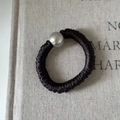 Detail of a black silk scrunchie with a polished silver metallic bead on linen texture - Black