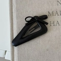 Detalle de una pinza de pelo de cuero negro con lazo sobre un fondo de tela beige - Forma Triangular (Lazo) / Negro