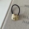 Close-up of cream marble resin charm on a dark brown elastic hair tie against a book - Milk Tea Textured (5#)