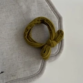 Detalle de un coletero de tela verde oliva con lazo sobre un fondo de lino gris claro - Lazo Amarillo Jengibre Coletero