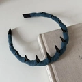 Dettaglio cerchietto in maglia blu scuro con denti antiscivolo neri appoggiato su libro - Blu lago