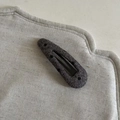 Detail eines kohlengrauen Wollstoff-BB-Clips mit gepunkteter Textur und Metallknopf - Graue Wassertropfen-Hohl-Punkt-Haarklammer