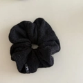 Close-up of black fuzzy knitted scrunchie texture with a small bow logo label detail - Black Plush Style