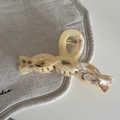 Dettaglio di un fermaglio per capelli tartarugato crema con design intrecciato su lino - Pinza a Croce Ondulata / Texture Ambra Gialla