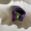 Detail view of a soft purple knitted headband featuring a 3D grape design and green leaf detail - Purple Hair Tie Grape