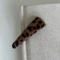 Detailansicht der Haarspange mit Leopardenmuster auf einem beigen Buchhintergrund - 3# Leopard Langes Dreieck Clip