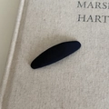 Detailed view of a black striped fabric oval hair clip resting on a beige textured book - Solid Blue Oval Clip