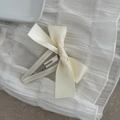 Detail view of a cream satin ribbon bow hair clip with a silver metal BB snap fastener - Off White