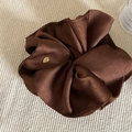 Detail of dark brown satin scrunchie with golden metal charm on a soft knitted background - Brown