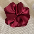 Detailed texture of burgundy satin scrunchie showing glossy fabric folds and soft sheen - Red