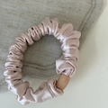 Dettaglio dello scrunchie in raso rosa con morbide pieghe e fibbia decorativa in legno - Elastico pieghettato rosa con perla cilindrica