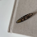 Detail einer Haarspange mit Schildpattmuster und goldenem Emblem auf Leinenstoff - Leopard Langer Streifen Gold-Etikett