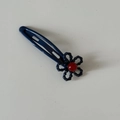 Detail of blue metal dog hair clip featuring a woven flower with a red center bead - Blue Clip with Blue Flower Red Dot