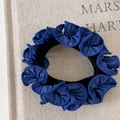 Donkerblauwe geruite scrunchie met ruches aan de rand op een beige achtergrond - Blauw Gegolfd Haarelastiekje